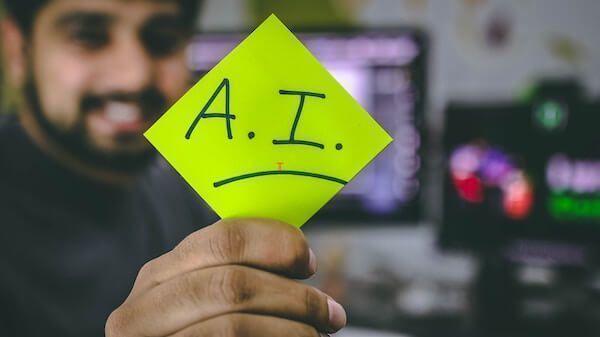 A.I. written on a green post it and held up by a smiling man